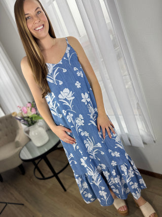 Woman wearing a blue floral dress standing indoors with white curtains in the background