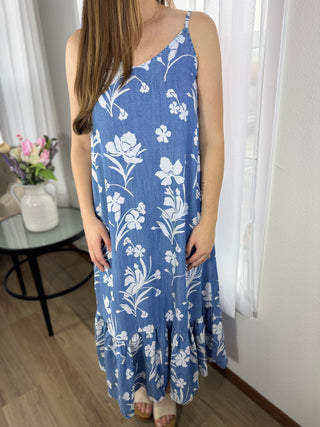 Woman wearing a blue floral dress in a room with white curtains and a small table with flowers.
