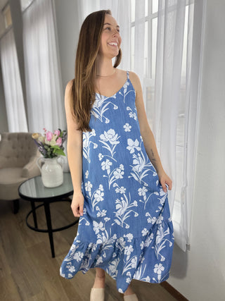Woman wearing a blue floral dress in a room with white curtains and a gray sofa.