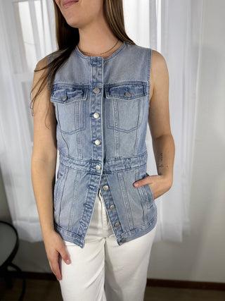 Person wearing a denim vest over a white top with a neutral background