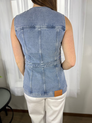 Person wearing a denim vest over a white shirt with a neutral background