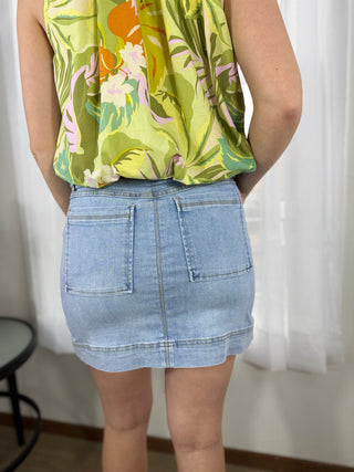 Person wearing a floral top and denim skirt against a white curtain background
