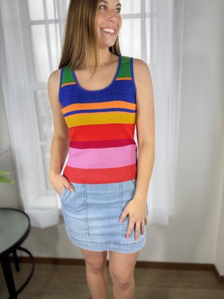 Woman wearing a colorful striped tank top and denim skirt indoors.
