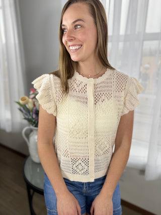Woman wearing a light-colored crochet top sitting indoors with a blurred background