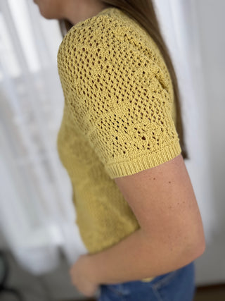 Yellow knitted top worn by a person against a white background