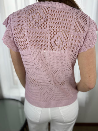 Pink crochet top worn by a person against a white curtain background