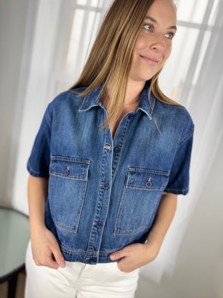 Woman wearing a blue denim shirt in a bright room with white curtains.