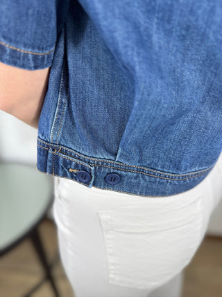 Close-up of a person wearing a blue denim shirt and white pants.
