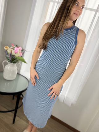 Woman wearing a blue and white striped dress in a bright room with a table and flowers.