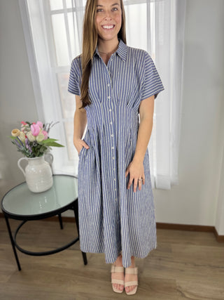 Woman wearing a blue and white striped dress standing in a room with a table and flowers.