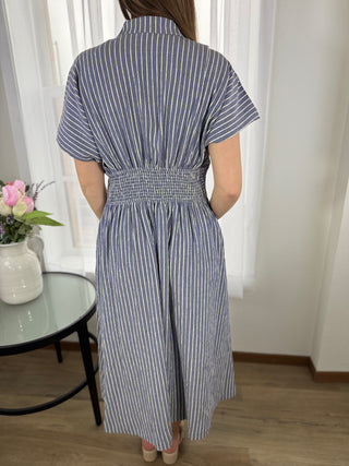 Woman wearing a blue and white striped dress in a room with a table and flowers.