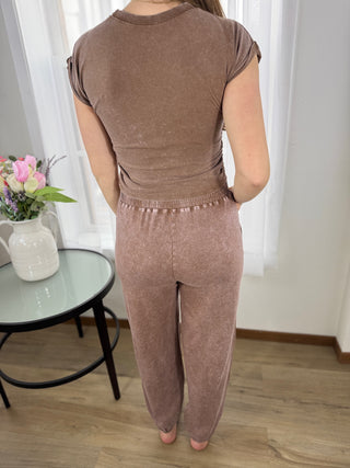 Person wearing a brown outfit standing in a room with a table and flowers in the background.