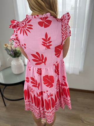 Pink dress with red floral patterns worn by a person, standing indoors.