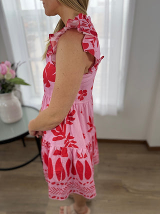 Woman wearing a pink dress with red floral pattern indoors.