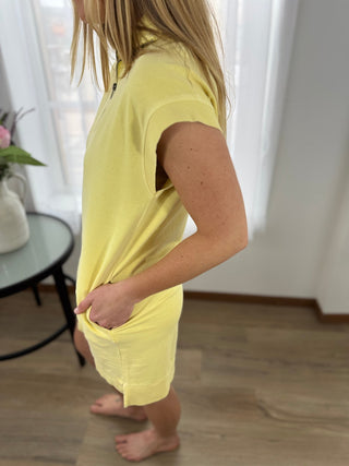 Person wearing a yellow outfit standing indoors with a neutral background