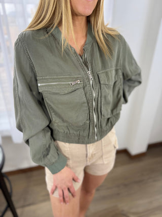 Person wearing a green jacket with zippers in a neutral setting