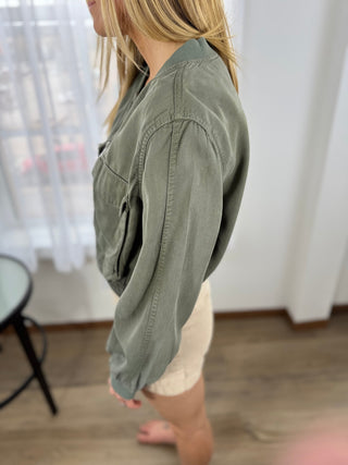 Person wearing a green jacket in a room with white curtains.