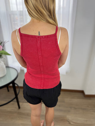 Person wearing a red tank top and black shorts in a room with white curtains.