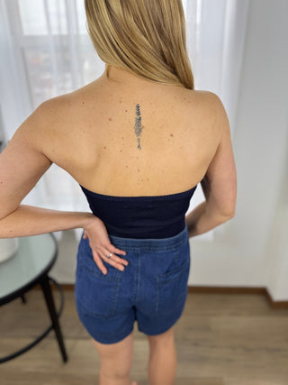 Person wearing a black strapless top and blue shorts with a tattoo on the back.