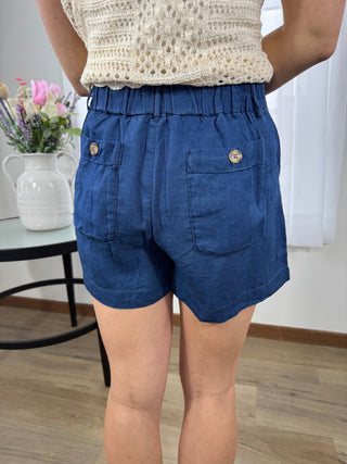 Person wearing blue shorts with a white top, standing indoors.