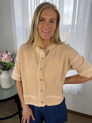 Woman wearing a beige checkered jacket indoors with a blurred background