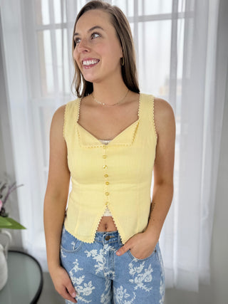 Woman wearing a yellow sleeveless top and blue floral pants indoors.