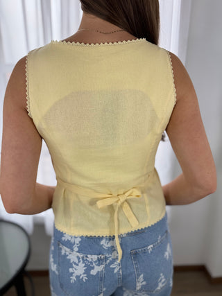 Person wearing a yellow sleeveless top with lace trim and blue floral pants against a white curtain background.