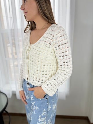 Woman wearing a white crochet top and light blue jeans indoors.