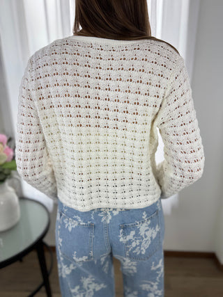 Person wearing a white crochet sweater and light blue jeans with floral patterns.