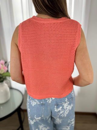 Person wearing a coral crochet top with a blurred background