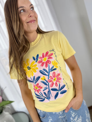Woman wearing a yellow t-shirt with colorful floral design against a white curtain background