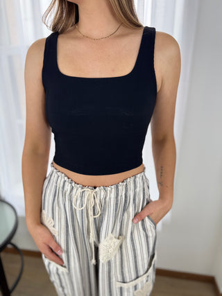 Person wearing a black tank top and striped pants against a white curtain background