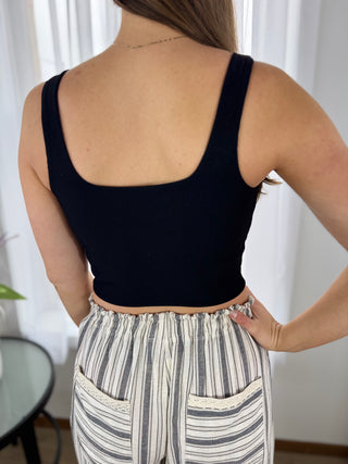Person wearing a black tank top and striped pants with a white curtain background