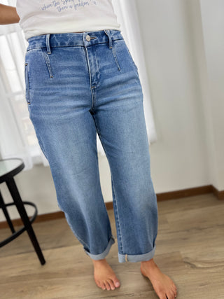 Person wearing blue jeans standing on a wooden floor with a white curtain in the background