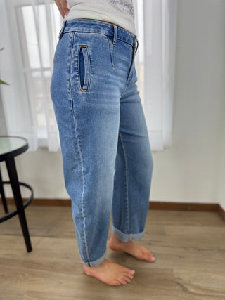 Person wearing blue jeans standing on a wooden floor with white curtains in the background