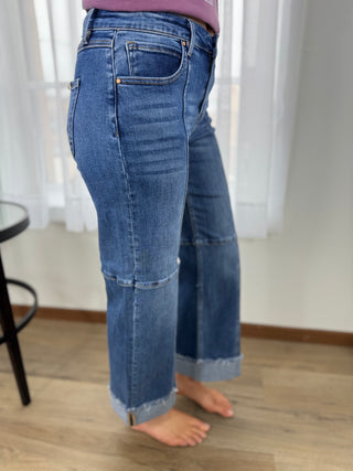 Person wearing blue jeans standing on a wooden floor with white curtains in the background