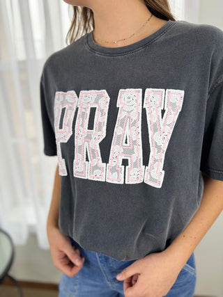 Person wearing a dark gray t-shirt with 'PRAY' printed on it, standing indoors.