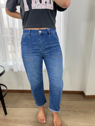 Person wearing blue jeans and a dark shirt with text, standing indoors.