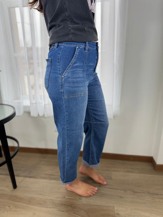 Person wearing blue jeans standing in a room with white curtains and a wooden floor.