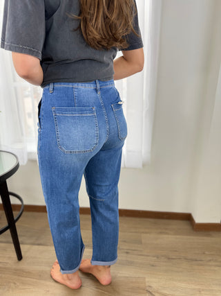 Person wearing blue jeans and a dark shirt in a room with white curtains.