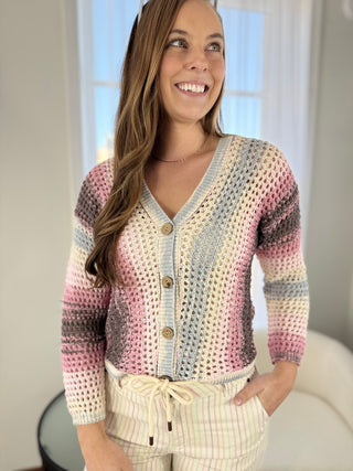 Woman wearing a colorful crocheted cardigan in a bright room.