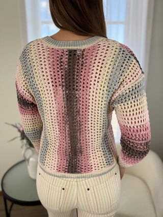 Person wearing a colorful crochet sweater in a room with a window and plant.