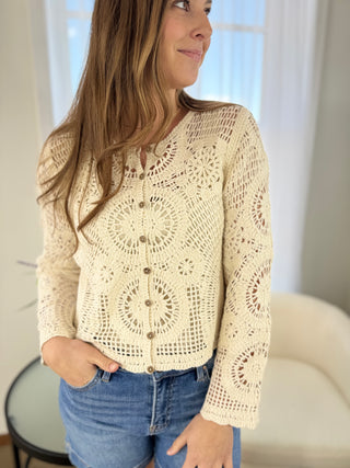 Woman wearing a beige crochet cardigan with a white background