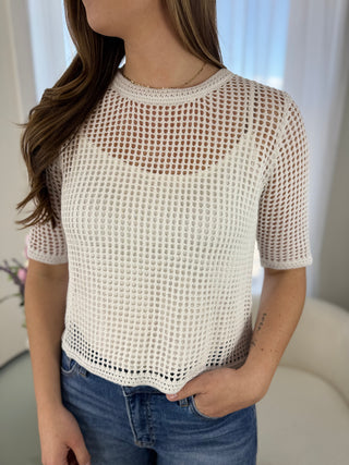 Woman wearing a white mesh top and blue jeans indoors.