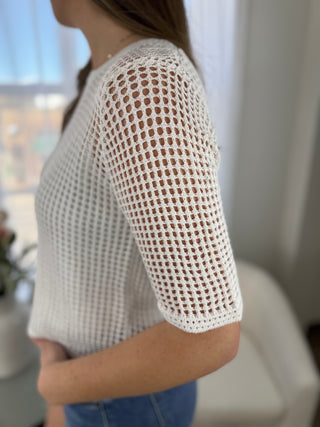 Person wearing a light-colored crochet top with a blurred background
