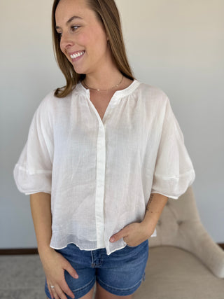 Woman wearing a white blouse and denim shorts against a neutral background