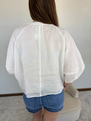 Person wearing a sheer white top and denim shorts in a minimal indoor setting