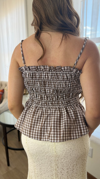A woman shown from the back wearing a brown and beige gingham smocked peplum top with thin spaghetti straps, paired with a cream lace skirt.