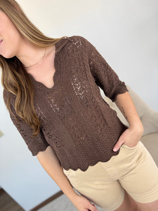 Woman wearing a brown lace top and beige shorts indoors.