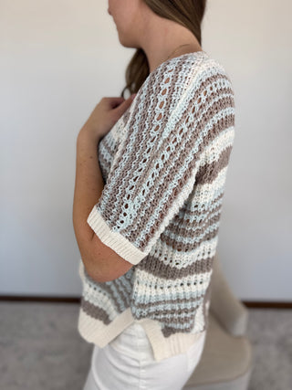 Woman wearing a striped crochet sweater against a plain background